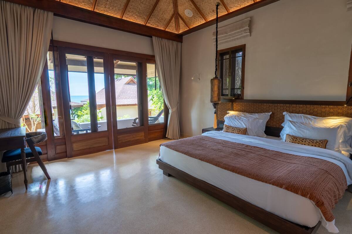 A spacious bedroom with a large bed, a desk, and a view of the outdoors.