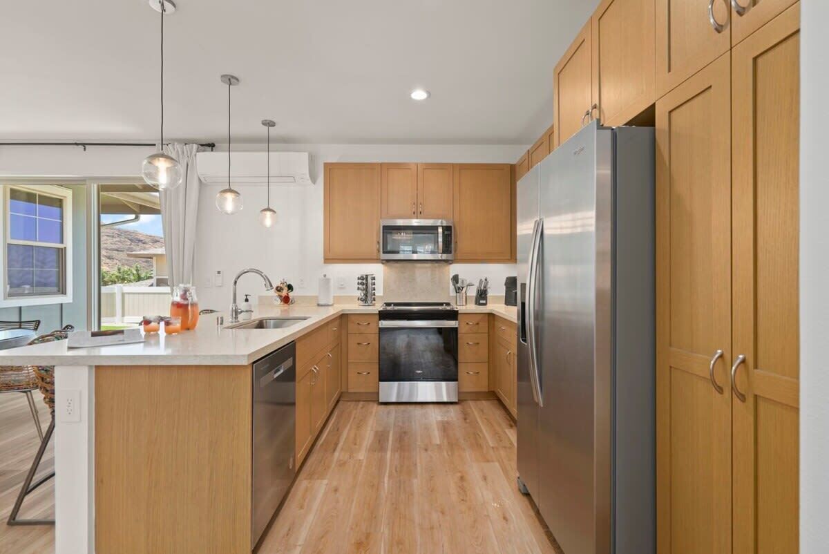Une cuisine moderne avec des meubles en bois, des appareils électroménagers en acier inoxydable et des luminaires suspendus.