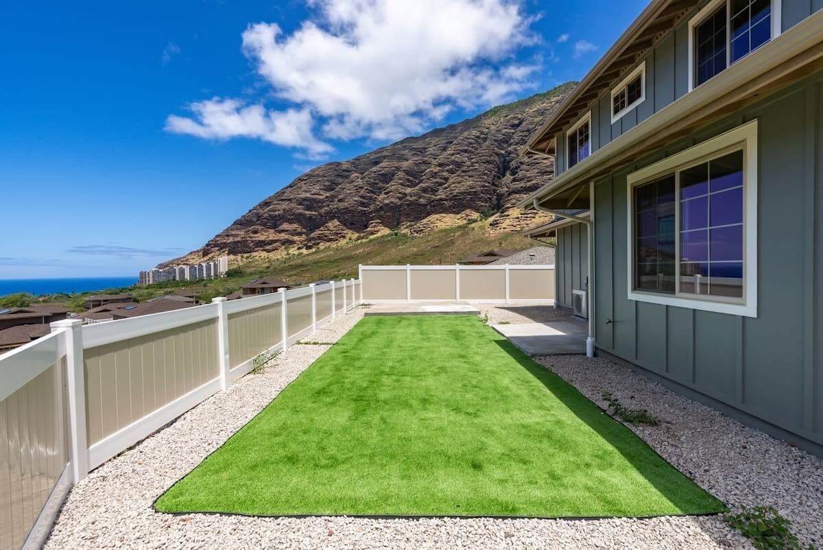 A rooftop patio with a green artificial grass area, white railing, and a view of a mountainous landscape.