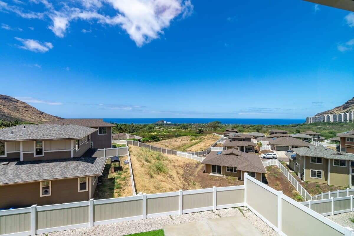 A residential area with houses, a fenced pathway, and a view of the ocean.