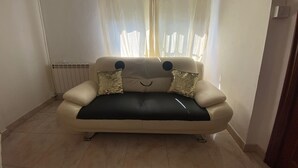 A beige sofa with two decorative pillows, a radiator, and a window with sheer curtains.