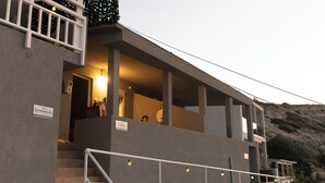 Un bâtiment moderne avec un escalier menant à un niveau supérieur. Des panneaux indiquent les différentes pièces ou zones, et une rampe se trouve devant l’escalier.