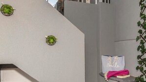 Un escalier avec un mur gris, deux petites plantes en pot, un coussin rayé et une serviette rose.