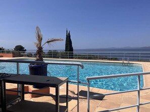 Uma piscina com grade de metal, uma palmeira e vista para o mar.