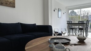 Ein modernes Wohnzimmer mit einem dunklen Sofa, einem Holztisch und einem Essbereich mit Tisch und Stühlen.
