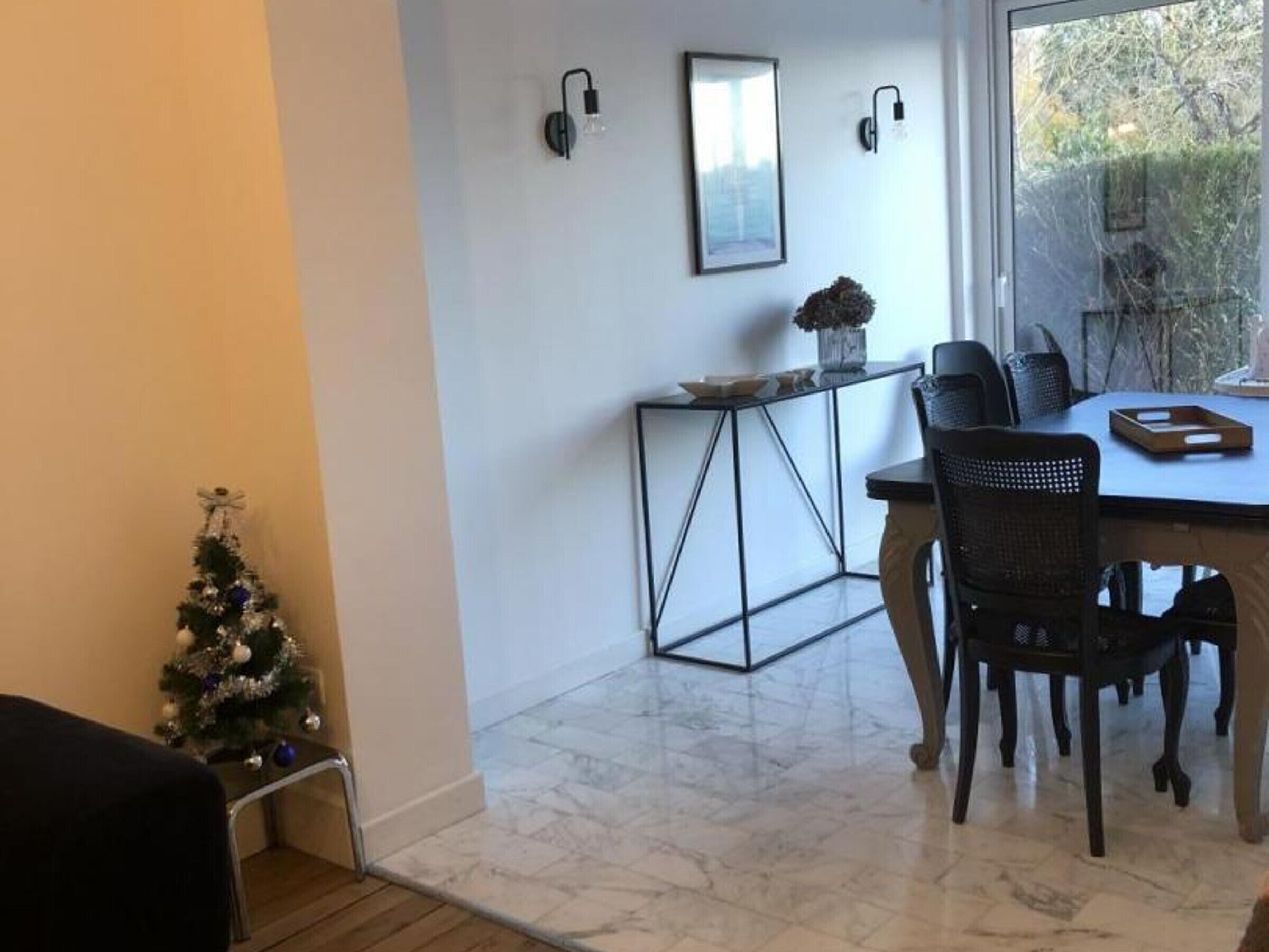 Un coin repas avec une table et des chaises, un petit sapin de Noël et une fenêtre donnant sur un paysage verdoyant.