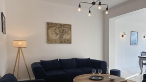 Ein modernes Wohnzimmer mit einem dunkelblauen Sofa, einem Holztisch mit Weingläsern, einer Stehlampe und einem Wandbild mit einer Karte.