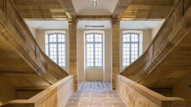 Eine steinerne Treppe mit hölzernen Geländern und großen Fenstern oben.