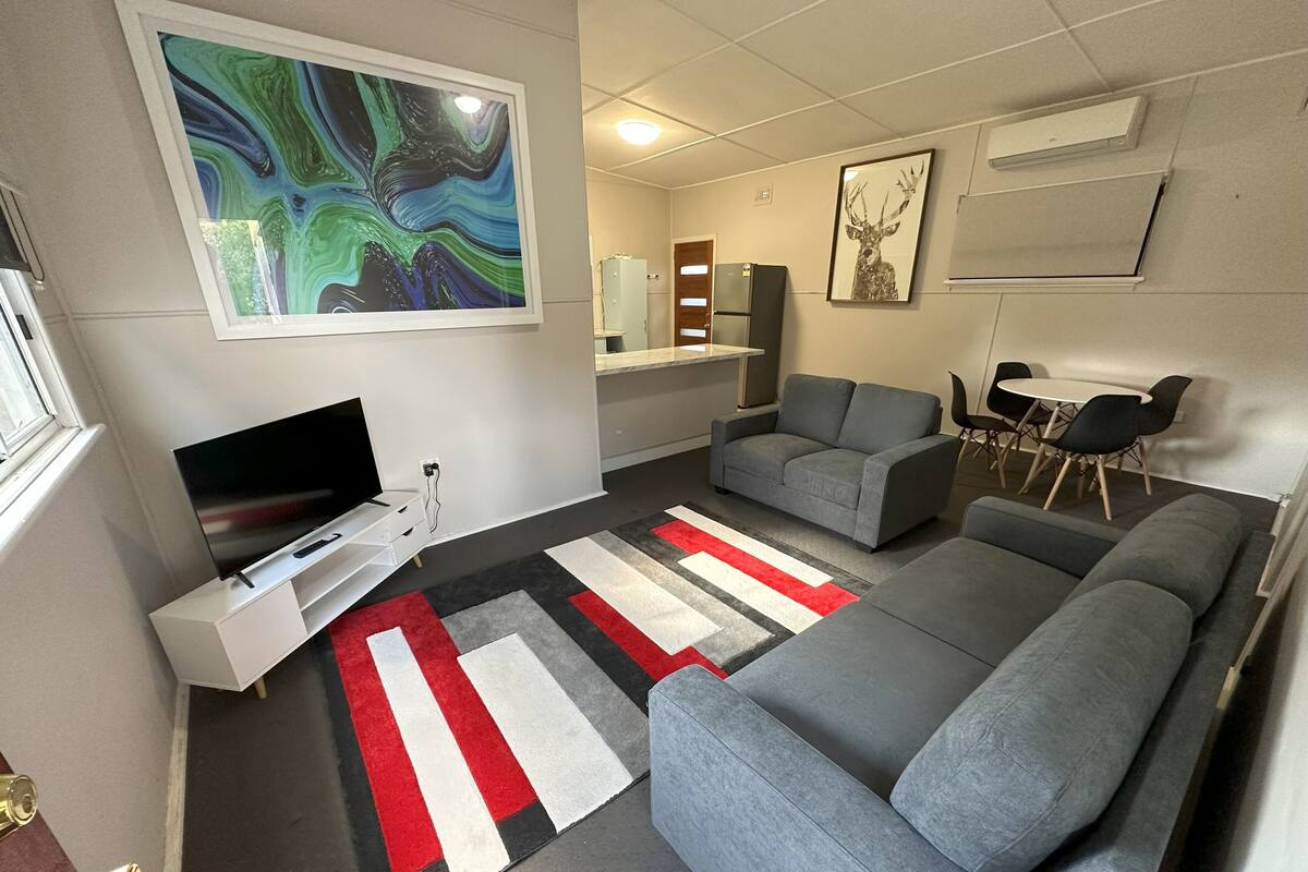 Un salon moderne avec un canapé gris, un téléviseur à écran plat, un tapis à rayures et un grand tableau abstrait.