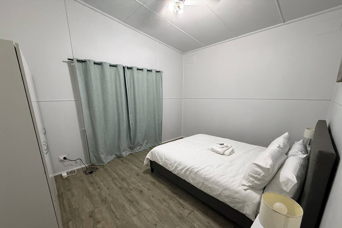 Une chambre à coucher avec un lit, des rideaux, une lampe de chevet et un plancher en bois.