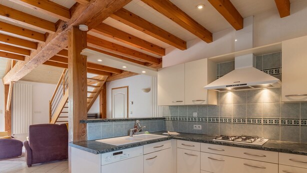 Une cuisine moderne avec des poutres en bois, une cuisinière à gaz, des armoires blanches et un dosseret carrelé.