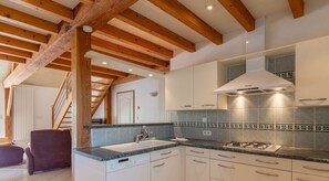 Une cuisine moderne avec des poutres en bois, une cuisinière à gaz, des armoires blanches et un dosseret carrelé.