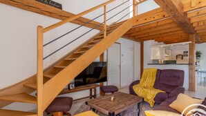 Un salon moderne avec un escalier en bois, un ensemble de canapés, une table basse et un téléviseur.