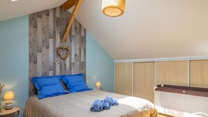 Une chambre avec un plafond en pente, un lambris en bois, un lit avec des coussins bleus, une lampe de chevet et un banc en bois.