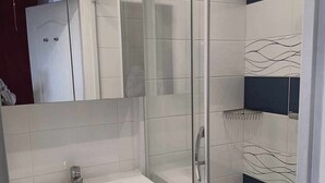 Uma casa de banho moderna com cabine de chuveiro em vidro, pia branca e porta-toalhas.