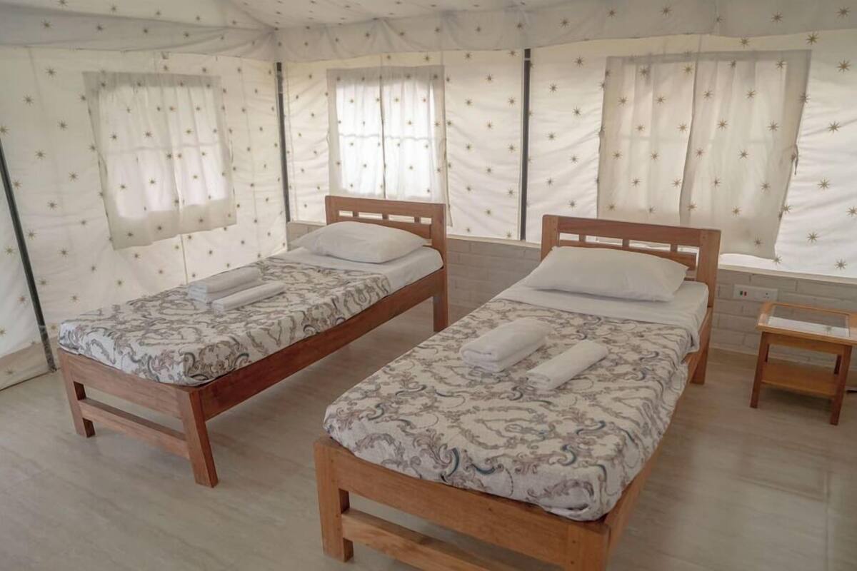 Quarto com duas camas de madeira, cada uma com roupa de cama estampada e almofadas brancas.