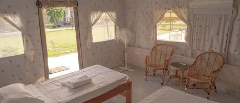 A tent-style room with two beds, a fan, wicker chairs, and a view of the outdoors.