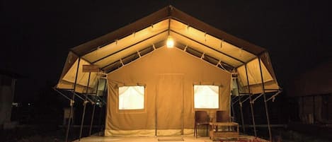 A tented accommodation with a central seating area, two windows, and a small outdoor space with steps and flowers.