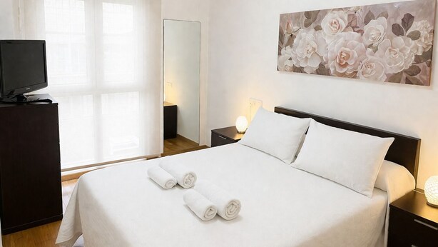 A hotel room with a bed, a TV on a dresser, a painting on the wall, and a window with curtains.