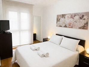 A hotel room with a bed, a TV on a dresser, a painting on the wall, and a window with curtains. - RELAX APARTMENT (Viveiro)
