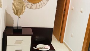 A modern interior with a dark wooden console, a white drawer unit, a decorative leaf, a round mirror, and a small shelf with a plant and a keychain.
