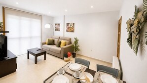 A modern living room with a sofa, a dining table set for four, and a TV on a stand.