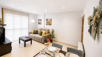 Un salon moderne avec un canapé, une table à manger pour quatre personnes et un téléviseur posé sur un meuble.