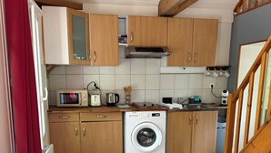 A compact kitchen with wooden cabinets, a washing machine, a microwave, and a table. - La Maison du Moulin (Saint-Georges-sur-Eure)