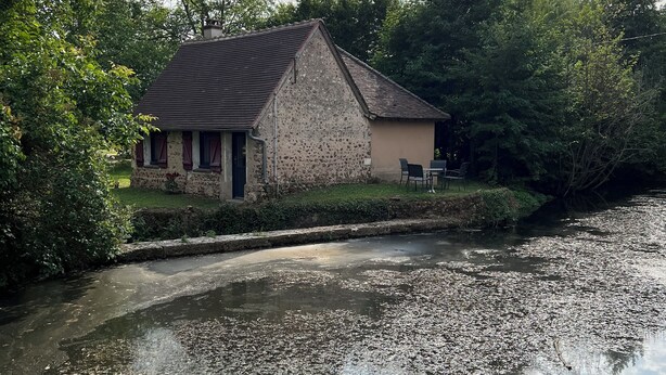 A rustic stone building with a sloped roof, situated beside a calm river. - La Maison du Moulin (Saint-Georges-sur-Eure)