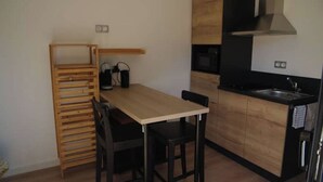 Una cucina compatta con un tavolo di legno, sedie nere, forno a incasso e lavello nero.