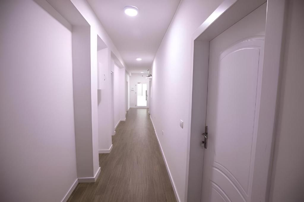 Un estrecho pasillo con paredes blancas y suelo de madera que conduce a una puerta al final.