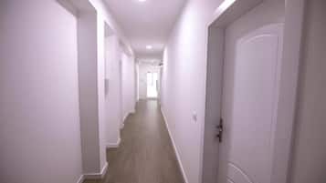 Un estrecho pasillo con paredes blancas y suelo de madera que conduce a una puerta al final.