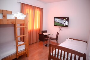 Habitación de hotel con literas, televisor, una pequeña mesa con sillas y un ventanal con cortinas.
