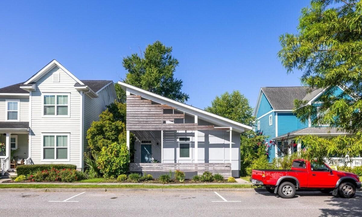 Una casa moderna de dos pisos con un porche cubierto, una camioneta roja estacionada al frente y un cielo azul despejado.