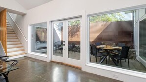 Ein modernes Interieur mit einer Treppe, einem Essbereich mit Tisch und Stühlen sowie großen Schiebeglastüren, die auf eine Außenpatio führen.