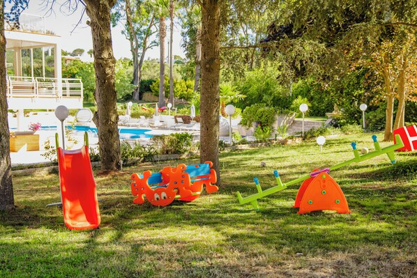 A playground with slides and swings, surrounded by trees and a pool. - Villa del Sole Martina Franca (Martina Franca)