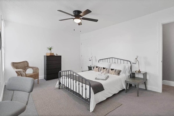 A bedroom with a bed, a dresser, a chair, a desk, and a ceiling fan.