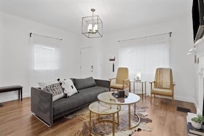 A modern living room with a grey sofa, two armchairs, a glass coffee table, and a chandelier.