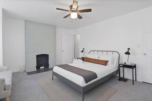 Ein Schlafzimmer mit Bett, Nachttischen, Deckenventilator, Kamin und einer Tür.