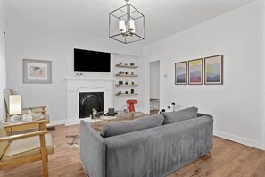 A modern living room with a grey sofa, a fireplace, a flat-screen TV, and a chandelier.