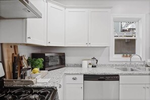 A kitchen with white cabinets, a granite countertop, a microwave, a sink, and a dishwasher.