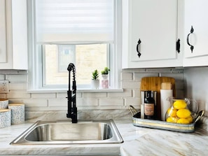 A kitchen with a stainless steel sink, a black faucet, and a window with blinds.
