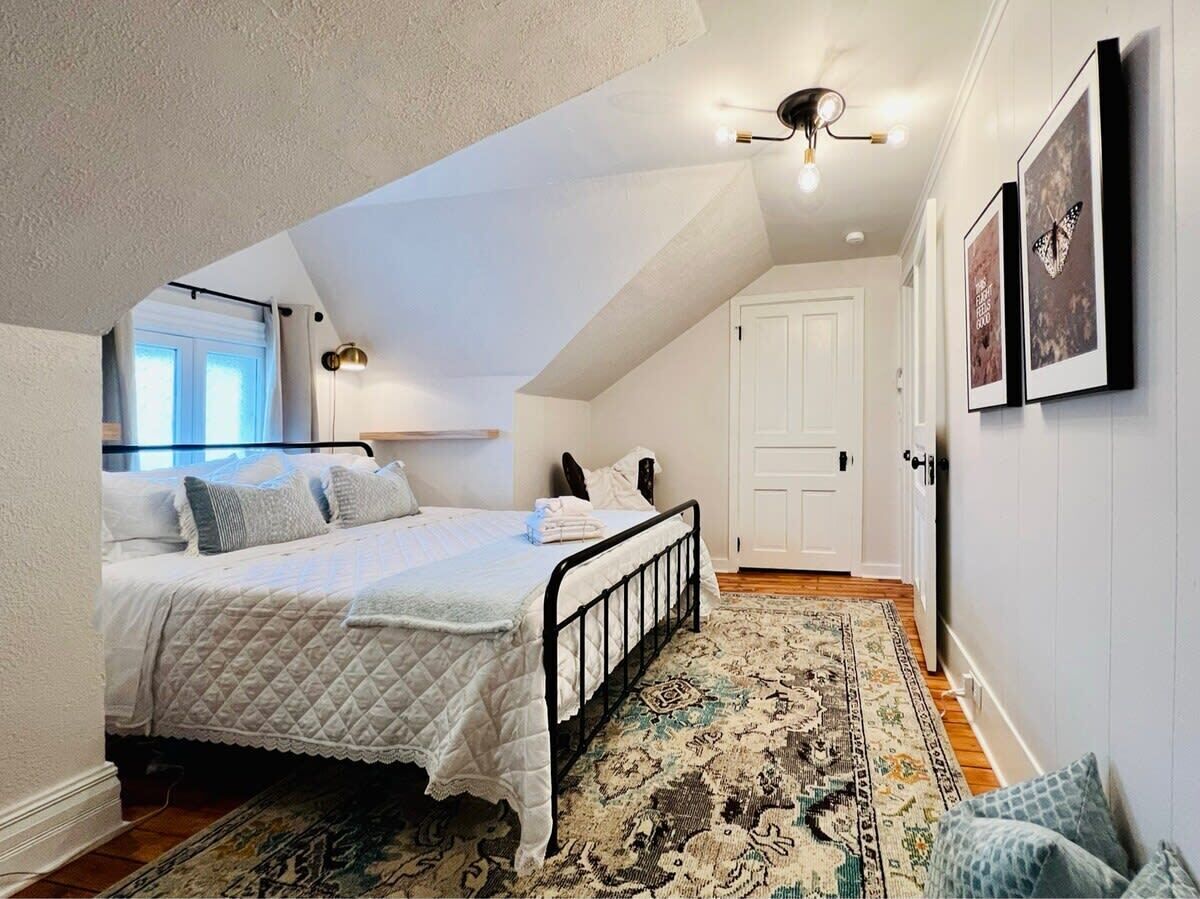 A bedroom with a bed, a patterned rug, a door, and wall-mounted artwork.