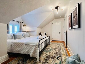 A bedroom with a bed, a patterned rug, a ceiling light, and framed pictures on the wall.