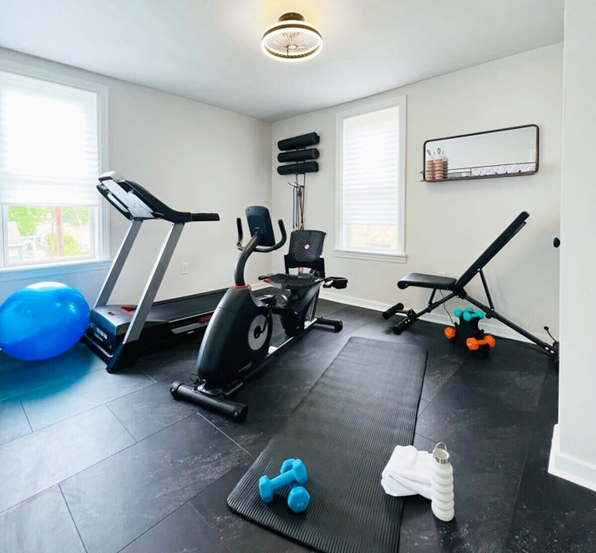 A home gym with a treadmill, elliptical, bench press, and dumbbells.