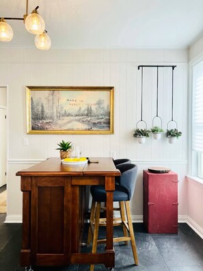 A kitchen with a wooden island, bar stools, a painting on the wall, and hanging plants.