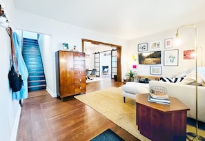 A living room with a staircase, wooden furniture, a sofa, a coffee table, and wall art.