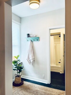 Um corredor com luminária, porta-toalhas na parede com uma toalha, uma planta pequena e um cesto no chão.