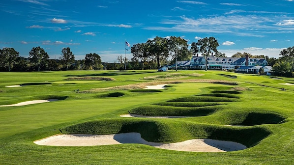 A golf course with bunkers, a flag, and a large building in the background.