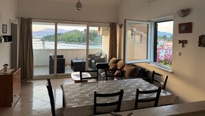 Un espace repas comprenant une table, des chaises et une vue sur un pont et des montagnes, visible à travers de grandes fenêtres.